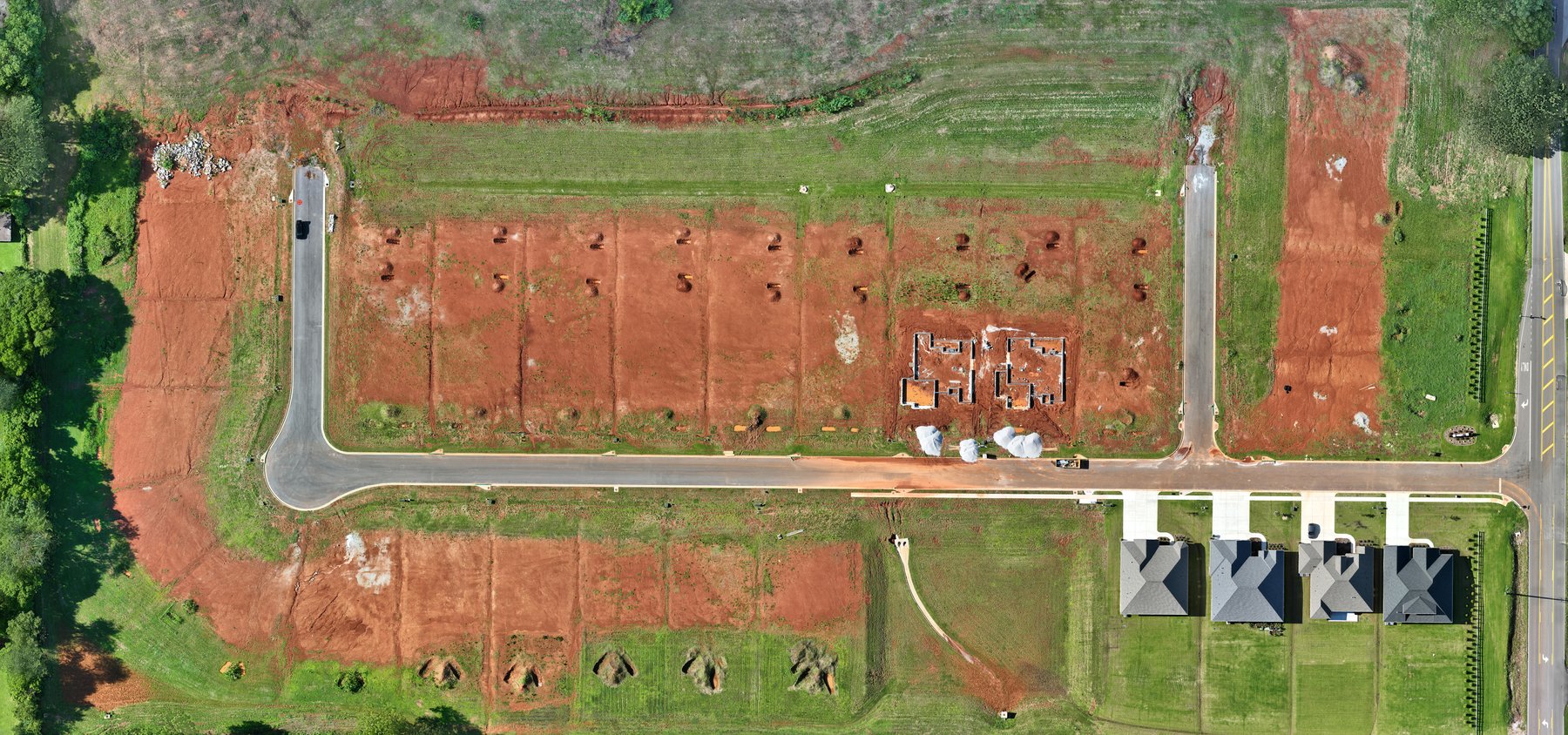 Wide top-down aerial progress map of a residential construction site showing roads, lots, foundations, and finished homes